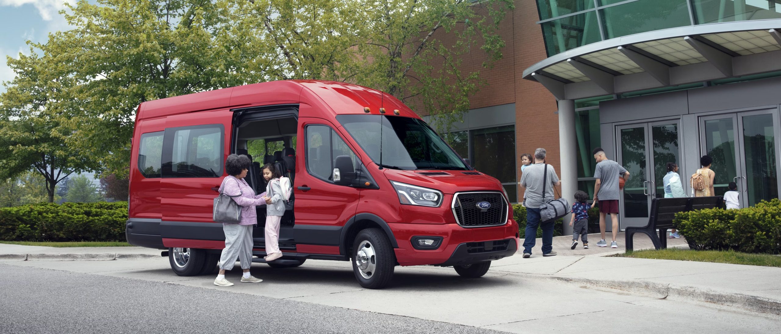 Red Ford Transit passenger van dropping off families outside a school or community center.