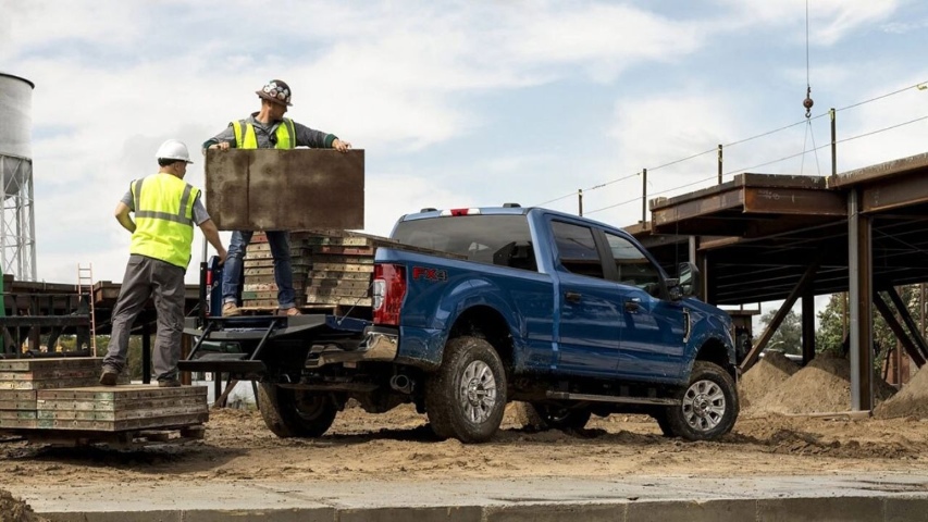 Workers loading materials into the bed of a blue 2026 Ford Super Duty at a construction site.