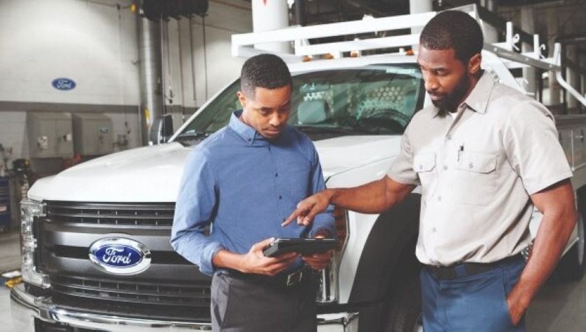 Two men reviewing a tablet in front of a Ford fleet truck during a commercial vehicle consultation.