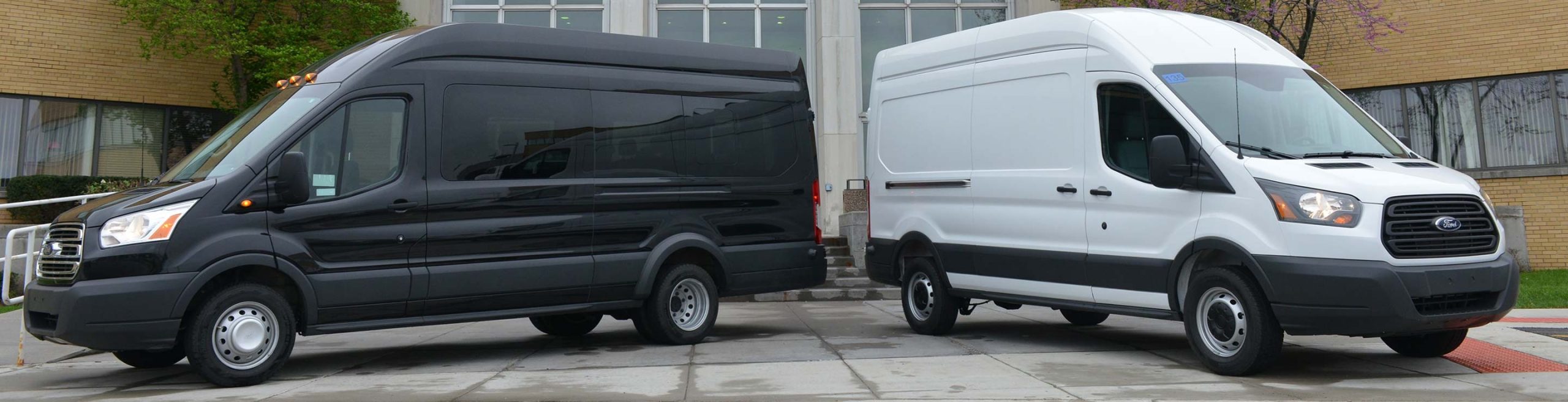 Black and white Ford Transit vans parked outside a modern brick building.