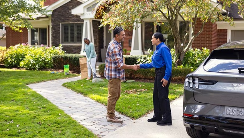 A local EV charger technician shakes hands with a homeowner in front of a Ford Mustang Mach-E parked in the driveway.