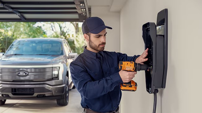 Technician installs a wall-mounted EV charger in a residential garage with a Ford F-150 Lightning parked in the background.