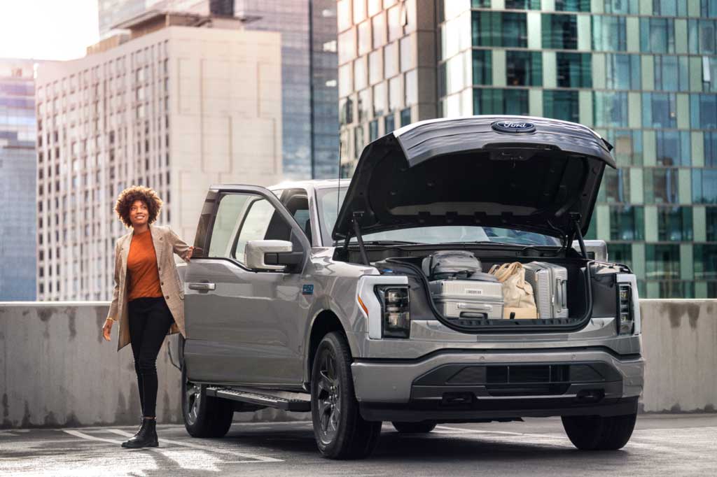 Woman standing beside a Ford F-150 Lighthing with its frunk open.